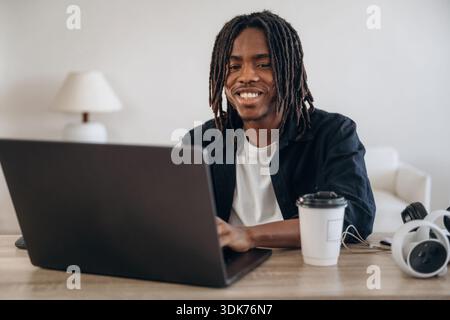 Young man is sitting by table with laptop and virtual reality glasses. Stock Photo