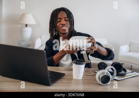 Wearing headset. Young man is sitting by table with laptop and virtual reality glasses. Stock Photo