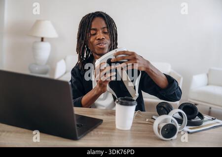 Wearing headset. Young man is sitting by table with laptop and virtual reality glasses. Stock Photo