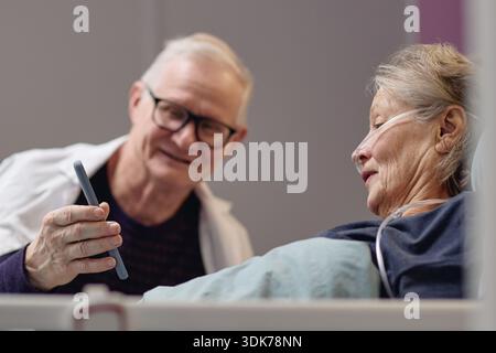 Senior Man Showing Smartphone to Elderly Woman in Hospital Stock Photo