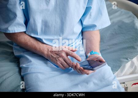 Middle Aged Man Using Digital Tablet While Sitting in Hospital Bed Stock Photo