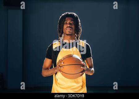 Relaxed, standing and posing. Young black man is playing basketball indoors. Stock Photo