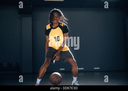 Dreadlocks hairstyle, active. Young black man is playing basketball indoors. Stock Photo