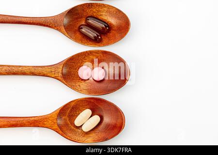 High angle view of various colorful vitamins, capsules, and dietary supplements in wooden spoons on a white background. Natural herbal medicine Stock Photo