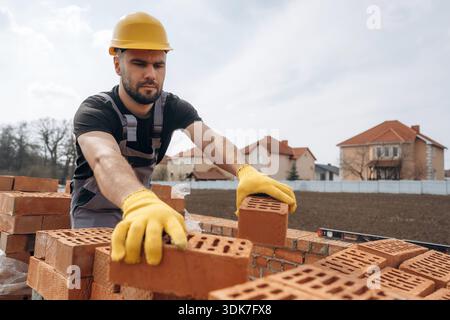 Work in progress. Construction man is at job with bricks outdoors. Stock Photo