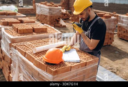 Plan on the paper. Construction worker is at job with bricks outdoors. Stock Photo