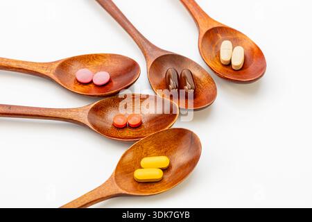 High angle view of various colorful vitamins, capsules, and dietary supplements in wooden spoons on a white background. Natural herbal medicine Stock Photo