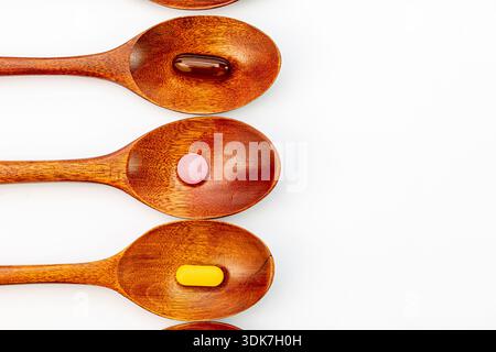 High angle view of single colorful vitamins and capsules in wooden spoons on a white background. Natural organic supplements and pharmaceutical Stock Photo