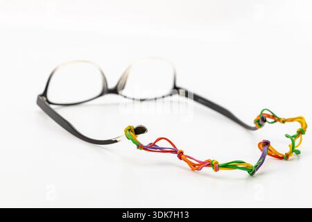 Stylish black eyeglasses with a creative DIY strap made from linked colorful rubber bands on a white background. Unique handmade eyewear accessory Stock Photo