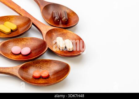 High angle view of various colorful vitamins, capsules, and dietary supplements in wooden spoons on a white background. Natural herbal medicine Stock Photo