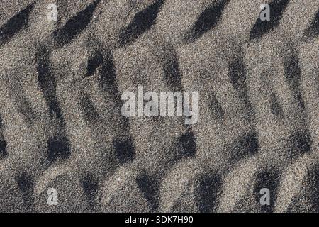 Detailed Texture of Vehicle Tire Tracks Imprinted on Dark Sandy Beach: Macro View of Patterned Sand Surface Under Direct Natural Sunlight Stock Photo
