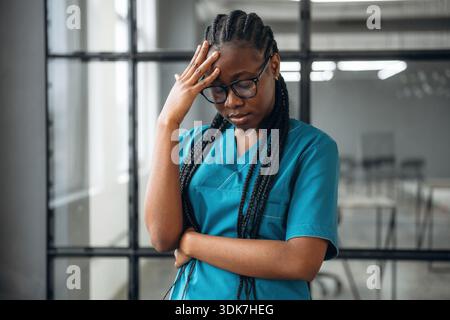 Exhausted, standing and feeling tired. Female doctor in coat is in the office clinic. Stock Photo