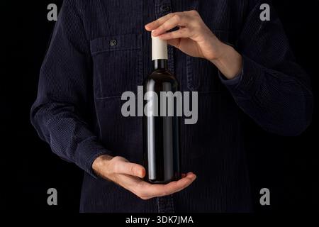 Man in blue shirt holding label-free wine bottle on black background. Ideal for mockups. Graphic label layout. online shop Stock Photo