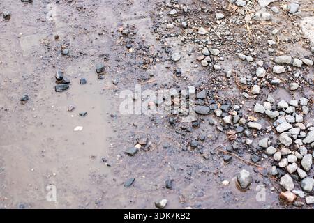 muddy gravel ground with scattered puddles, closeup view of small pebbles and coarse stones mixed with clay, shallow Stock Photo