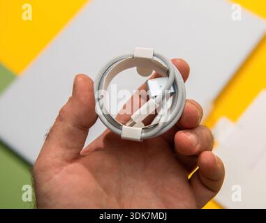 Paris, France - Mar 13, 2025: Closeup of a hand holding a braided USB cable from MacBook Air unboxing on bright geometric background showcasing clean Stock Photo
