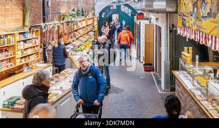 Freiburg, Germany - Feb 10, 2025: Busy Freiburg old market hall interior with shoppers walking past colorful fruit stalls, brick walls, deli counters Stock Photo