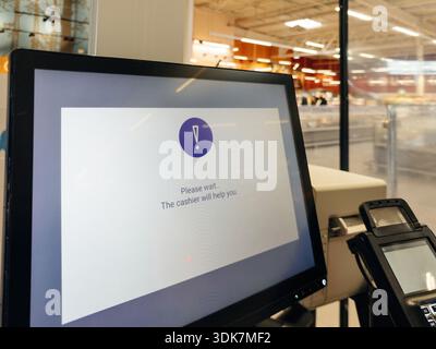 Self service checkout screen in a supermarket displaying a please wait message while the cashier is called to assist the customer during a shopping tr Stock Photo