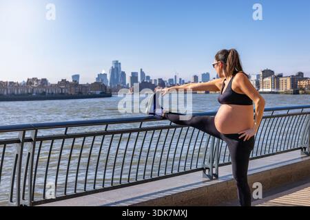 A sportive, pregnant woman doing her fitness exercises outdoors in front of a city skyline Stock Photo
