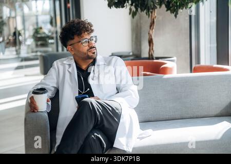 Holding paper cup of drink, break. Doctor is indoors in the modern building. Stock Photo