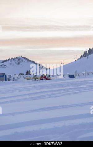 View of snow-covered ground with red and yellow snow groomers under the pastel sky, surrounded by snow-capped mountains, Morgins, Valais, Switzerland. Stock Photo