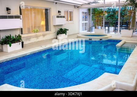 St. Paul's, Malta - January 25, 2026: Indoor swimming pool with blue tiles and a jacuzzi in a hotel relaxation area with doors leading to a terrace. Stock Photo