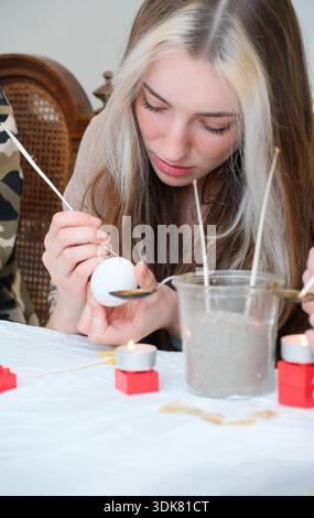 Young woman painting traditional easter eggs indoors using wax and candles focused on careful handwork expressing patience tradition creativity and qu Stock Photo