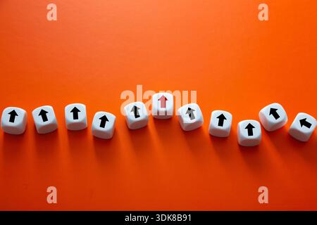 White dice with black arrows and one red arrow on an orange background Stock Photo