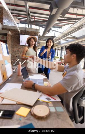 Diverse coworkers collaborating at table in creative office using laptop, pencil and color swatches. Collaboration, brainstorming, startup, modern, workspace, innovative, team || Model released Stock Photo