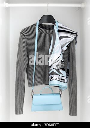 Minimalist wardrobe interior with grey ribbed sweater, patterned scarf and light blue handbag on hanger. Neutral fashion concept, capsule wardrobe, mo Stock Photo