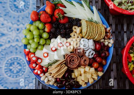 Colorful summer charcuterie board with fresh fruit, cheese, crackers and cured meats arranged on a blue plate. Stock Photo
