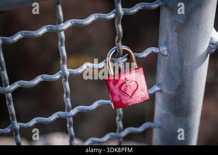 Rusty red padlock with engraved heart on railing, symbolising lonely unrequited love, heartbreak, abandonment, emotional pain, relationship concept. Stock Photo