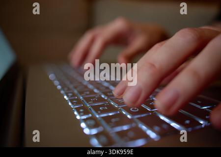 Close up of hands typing on backlit laptop keyboard in dim light. Concept of remote work and online communication Stock Photo