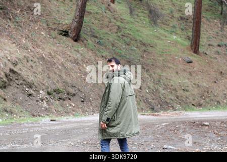 A man walking on a forest road in nature, wearing a green jacket. Concept of outdoor lifestyle, travel, freedom and calm mood. Stock Photo