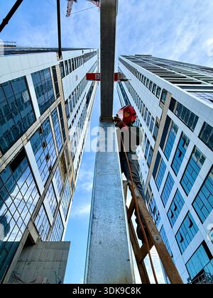 Professional welder in safety mask welding steel beams on a high-rise construction site. Low-angle view with industrial crane and modern buildings. Stock Photo
