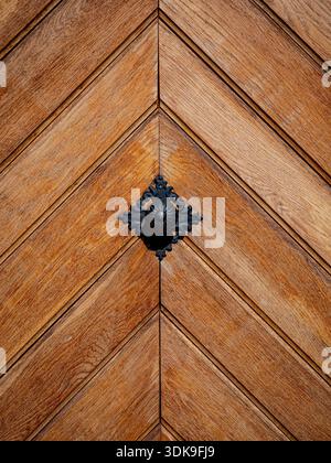 Chevron-pattern wooden door with central decorative black metal ornament. Stock Photo