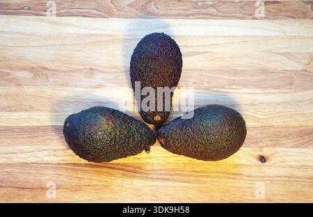 Top view flat lay of fresh whole Hass avocados arranged on a wooden cutting board. Minimalist food composition with natural light, organic composition. Stock Photo