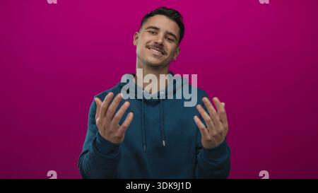 Young hispanic man gestures come here with hands against a vibrant pink background, appearing inviting and playful in a vivid, isolated studio shot. Stock Photo