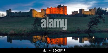 A panoramic view at dusk of Alnwick Castle in Northumberland reflected in the river Aln as seen from the Pastures with lovely reflections and a clear Stock Photo