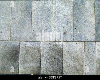 Top down view of wet grey stone pavement tiles in Budapest. Detailed texture of damp granite flooring with small puddles on a rainy day in the Zuglo d Stock Photo