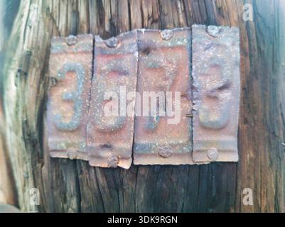 Macro view of rusty metal plates nailed to a dark wooden utility pole in Budapest. Features embossed numbers 3673 with heavy oxidation and weathered i Stock Photo