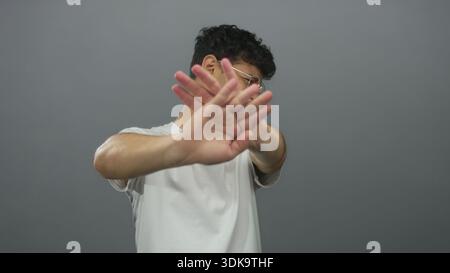 Young hispanic man shielding face with raised hands in blocking gesture against a gray studio wall; denial. Stock Photo