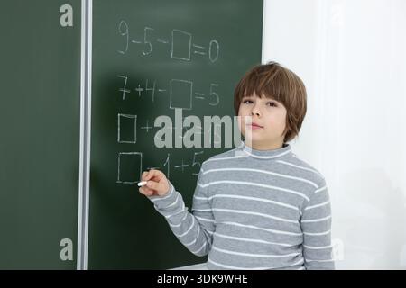 Schoolboy doing math on chalkboard in classroom Stock Photo