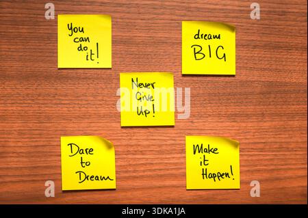 Five green sticky notes arranged on a wooden surface, each featuring a handwritten motivational message in black marker. The notes include phrases lik Stock Photo