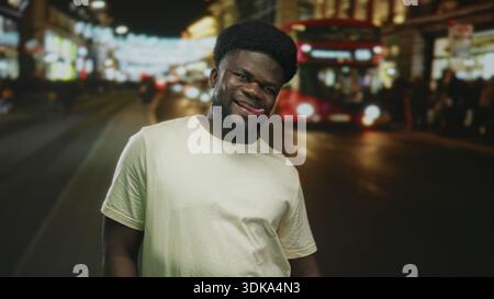 Man sticks tongue out and smiles on a busy neon lit city street with a double decker bus at night; playful urban confidence. Stock Photo