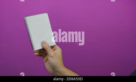 Male hand holding notebook against vivid pink background, showcasing stationery in minimalist setting, highlighting simplicity and focus of isolated o Stock Photo