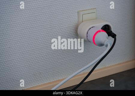 Smart power plug with glowing red indicator connected to wall socket representing electricity usage energy control and modern home technology concepts Stock Photo