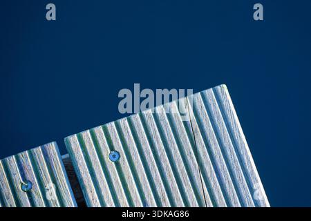 A tight view shows the corner of a wooden bench with carved grooves, set against a smooth blue background, emphasizing geometry, texture, and weathere Stock Photo