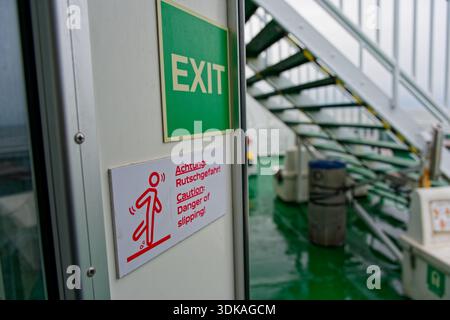 On the ship deck an Exit label sits beside a slipping figure icon, with warnings Achtung Rutschgefahr in german, means Danger of slipping to help prev Stock Photo