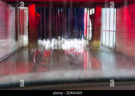 View through windshield inside automated car wash with brushes steam water and red light reflections creating a dynamic abstract scene for automotive Stock Photo