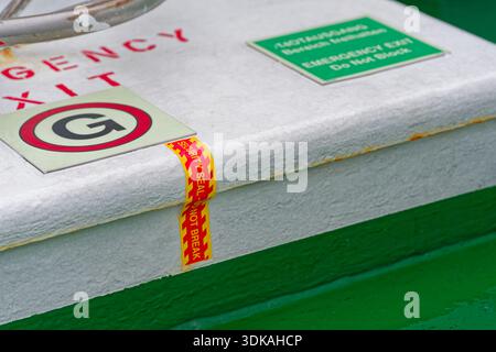 A metal emergency exit cover shows warning labels and intact seal tape, indicating the hatch has not been opened and should stay clear for safety use. Stock Photo
